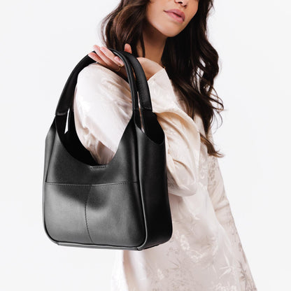 Pebbled--Black*Medium | A model holding a u-shaped, flat-bottomed leather shoulder bag with two outside pockets