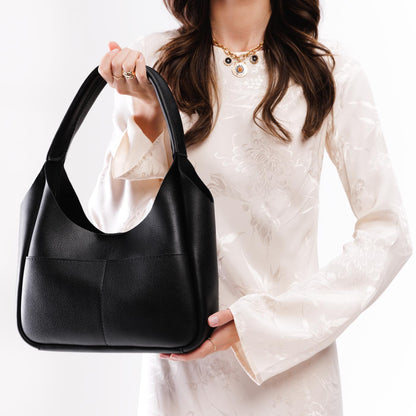 Pebbled--Black*Medium | A model holding a u-shaped, flat-bottomed leather shoulder bag with two outside pockets