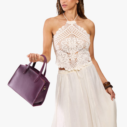 Plum*Medium | Model carrying leather tote bag with handles, adjustable crossbody strap, and two back pockets