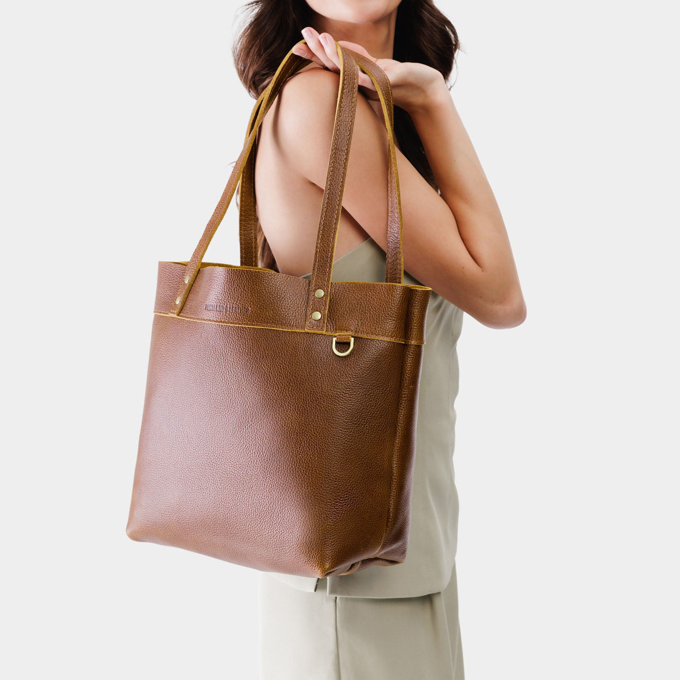 Asheville*Medium*Classic | Model holding a leather tote bag with riveted straps and exterior key loop