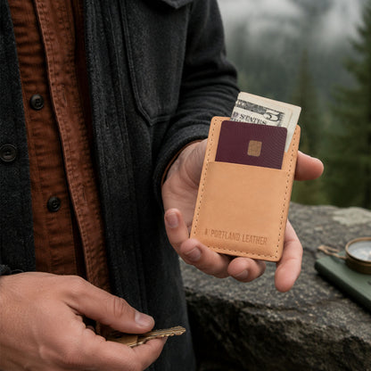 Naturale | A model outdoors holds a tan leather card holder in front of a stone wall