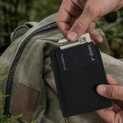 Nero | A close-up of a black leather card holder wallet being held in front of backpack.