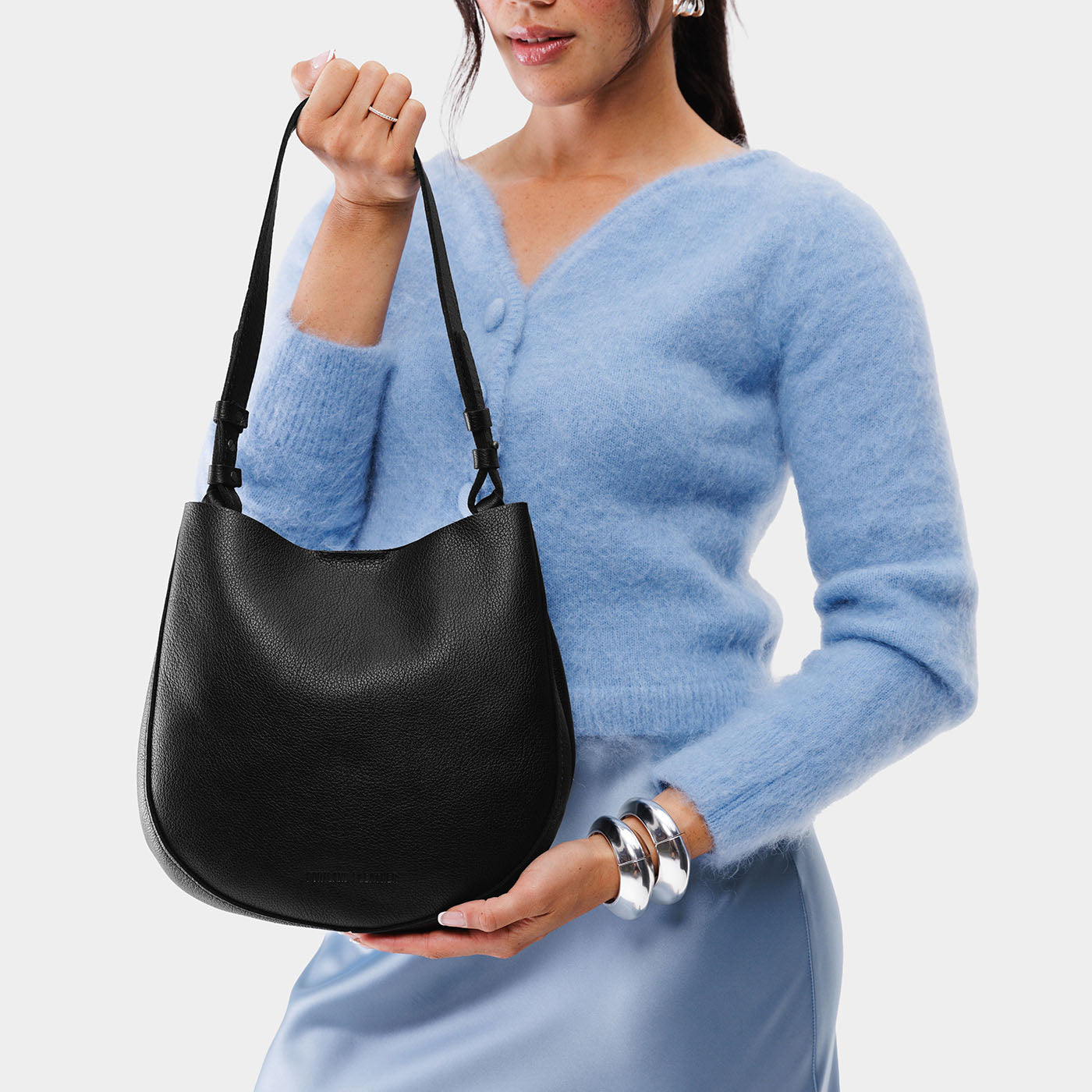 Pebbled--black*Medium | Woman wearing rounded shoulder bag with adjustable strap on a white background