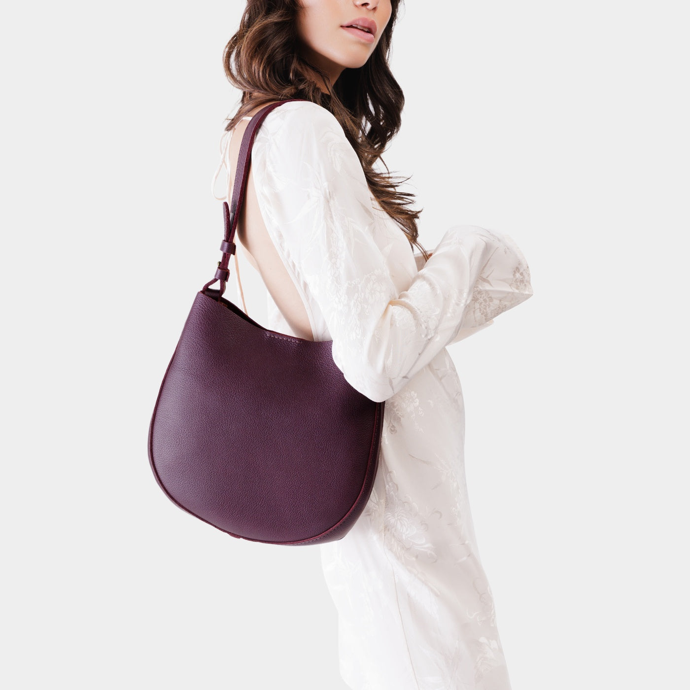 Plum*Medium | Woman wearing rounded shoulder bag with adjustable strap on a white background