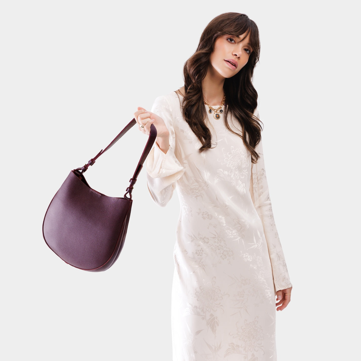 Plum*Medium | Woman wearing rounded shoulder bag with adjustable strap on a white background