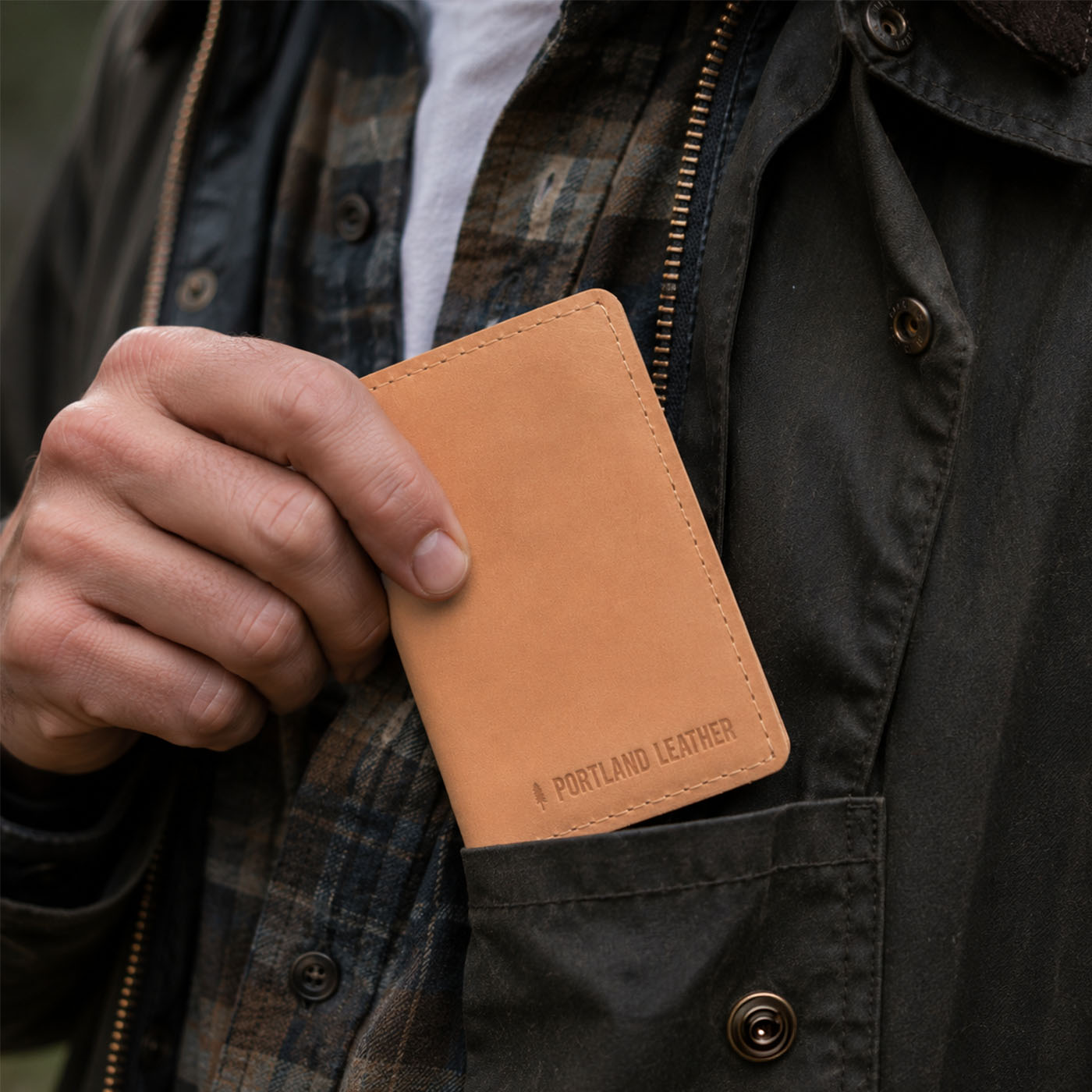 Naturale | A close-up of a model sliding a leather card holder into their shirt pocket