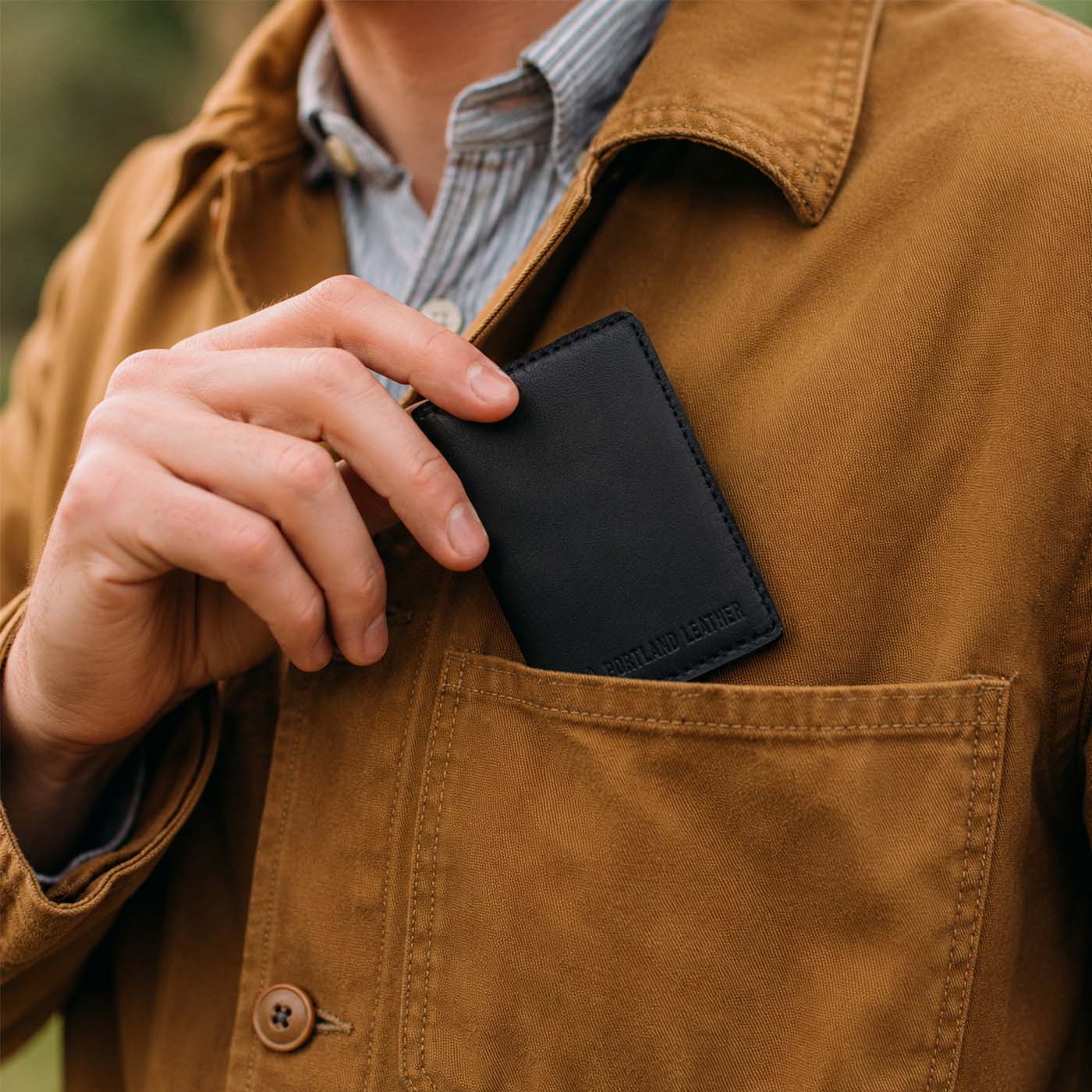 Nero | A close-up of a model sliding a leather card holder into their shirt pocket