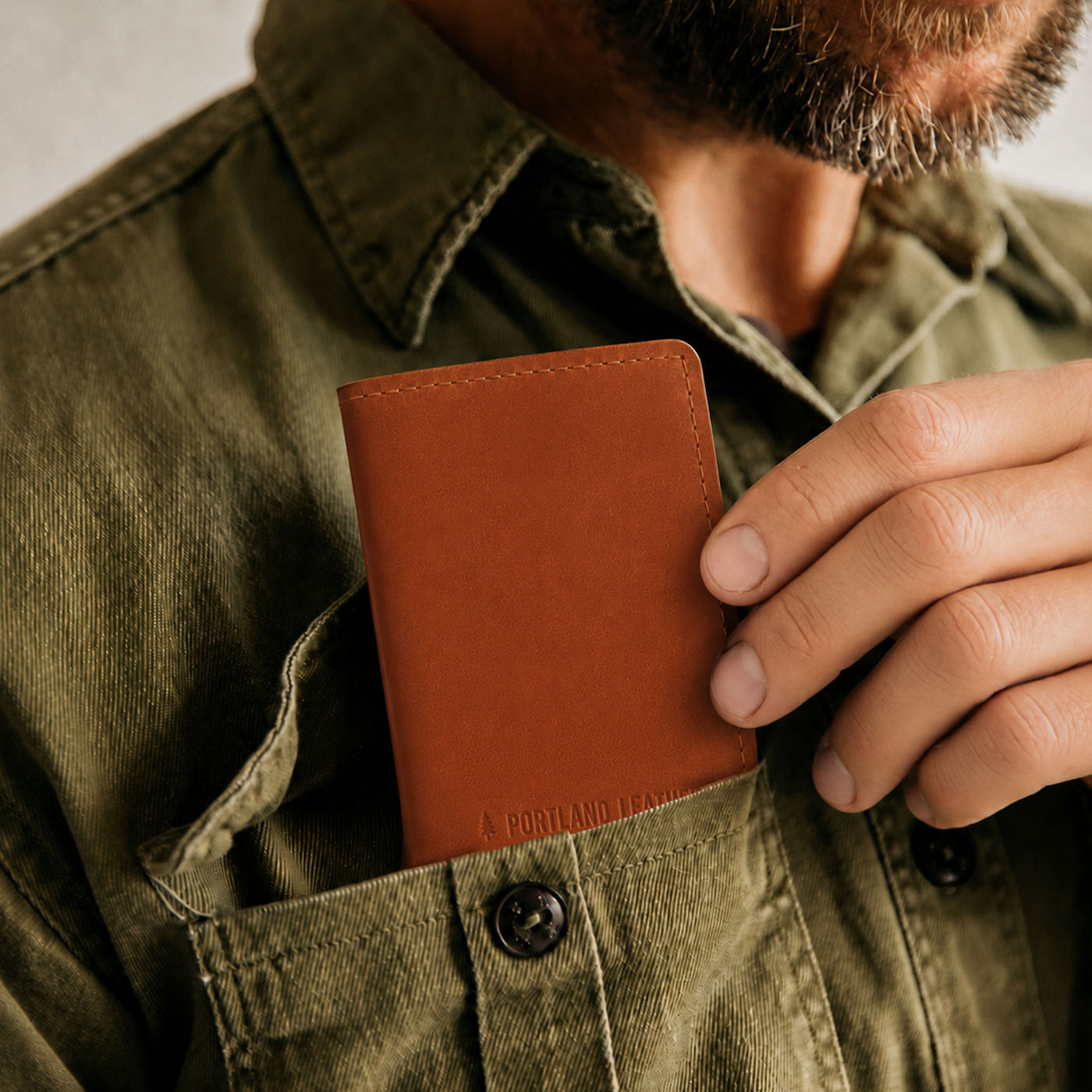 Toscano | A close-up of a model sliding a leather card holder into their shirt pocket