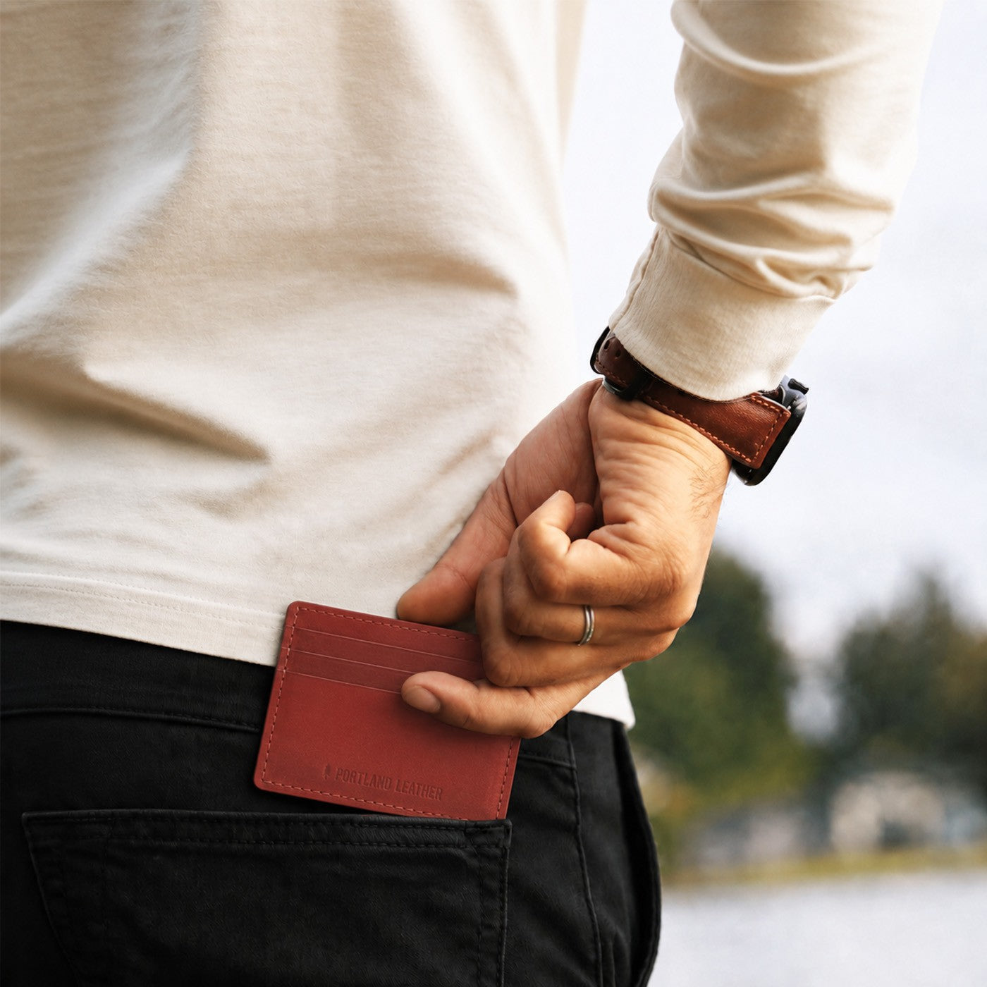Marrone | A close up of a model sliding a leather card holder into their back pants pocket