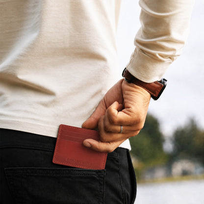 Marrone | A close up of a model sliding a leather card holder into their back pants pocket