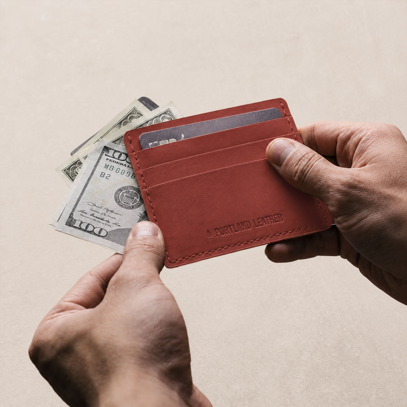 Marrone | A card holder held by two hands over a light wood table, with a credit card and money