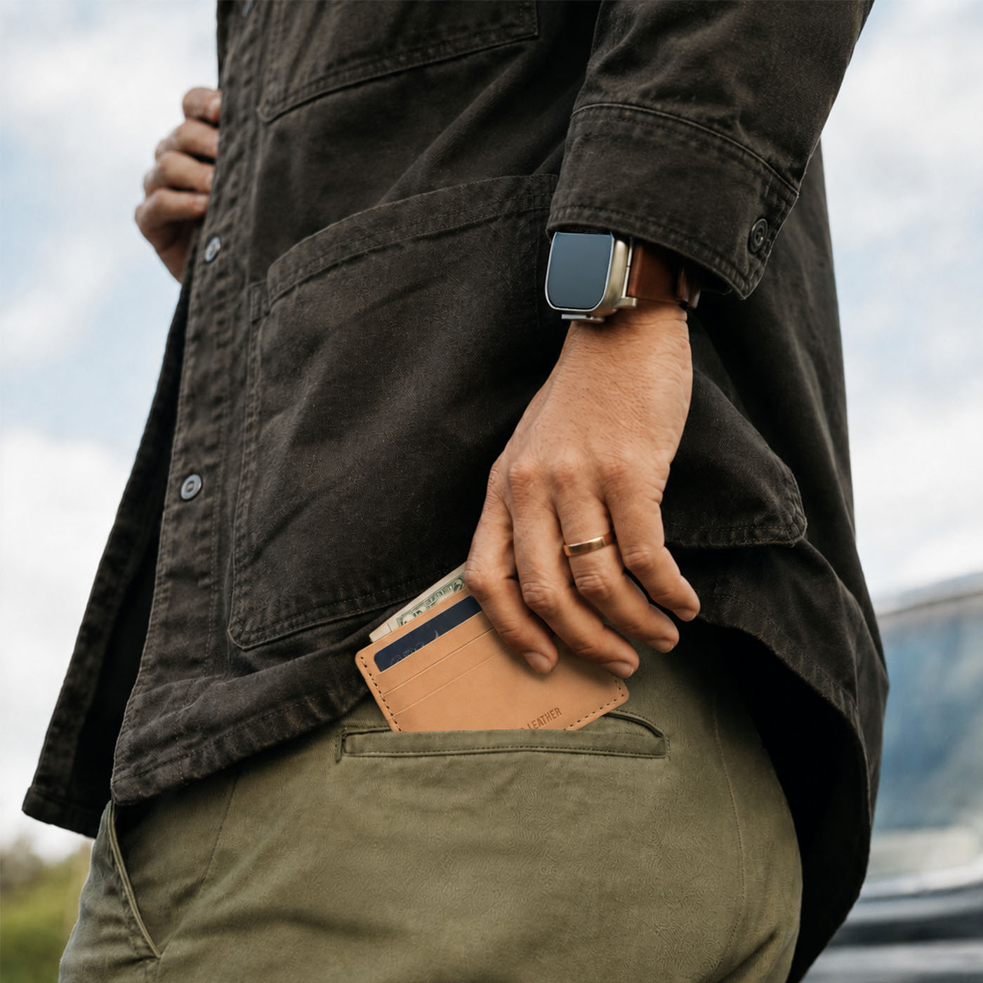 Naturale | A close up of a model sliding a leather card holder into their back pants pocket