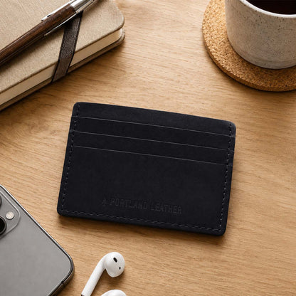 Nero | A leather card holder styled on a wooden desk with a notebook, pen, earbud case, phone, and coffee cup