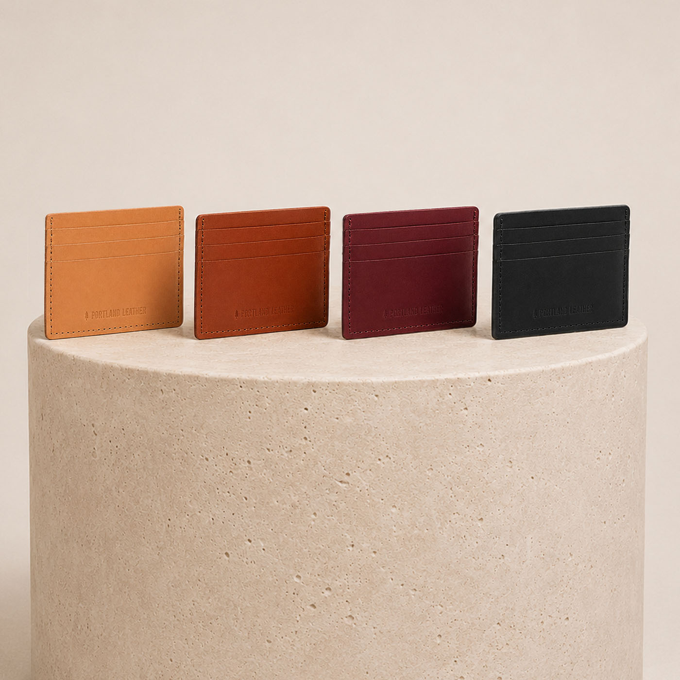 Nero | Group of wallets lined up on top of a textured beige stone cylinder