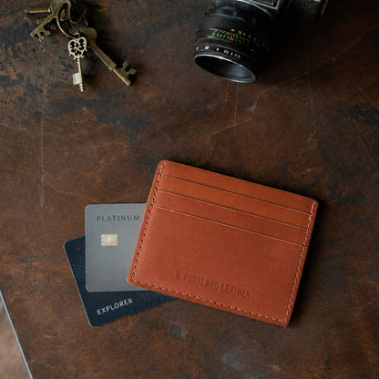 Toscano | A leather card holder styled on a dark textured surface with credit cards, keys, and a camera lens