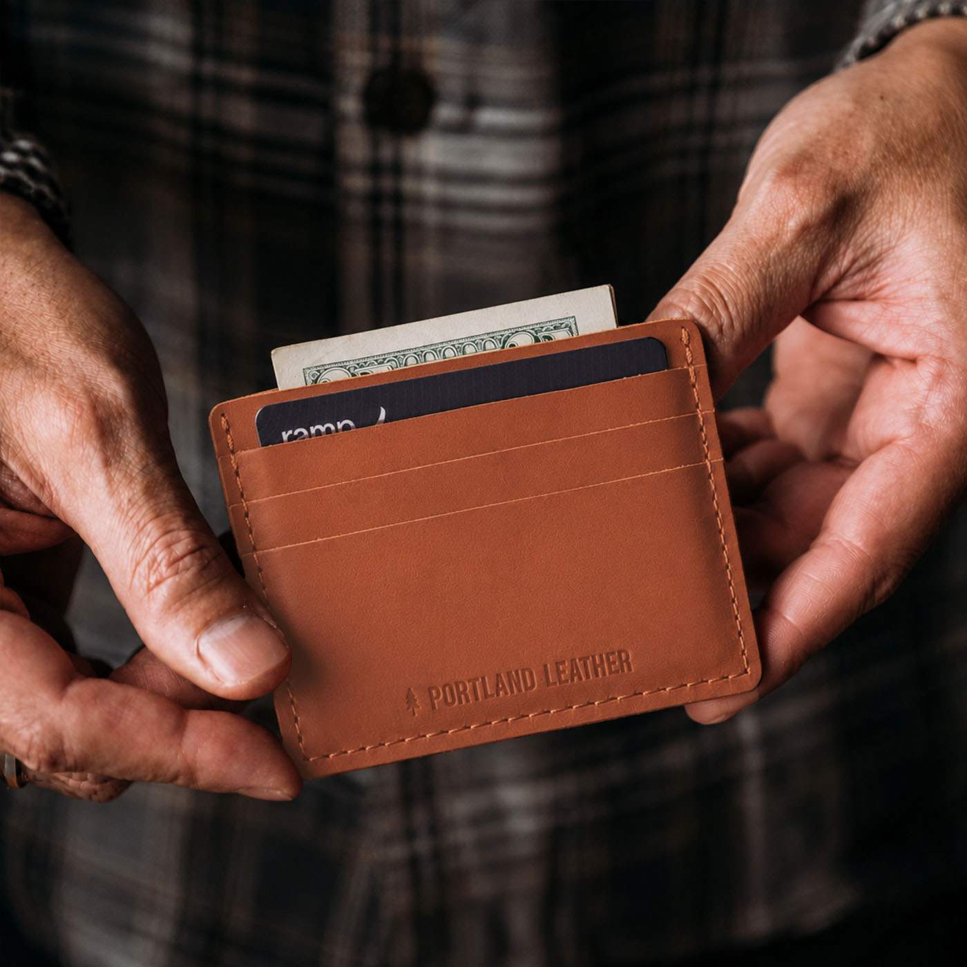 Toscano | A close-up lifestyle shot of a model holding a leather card holder with money and card inserted