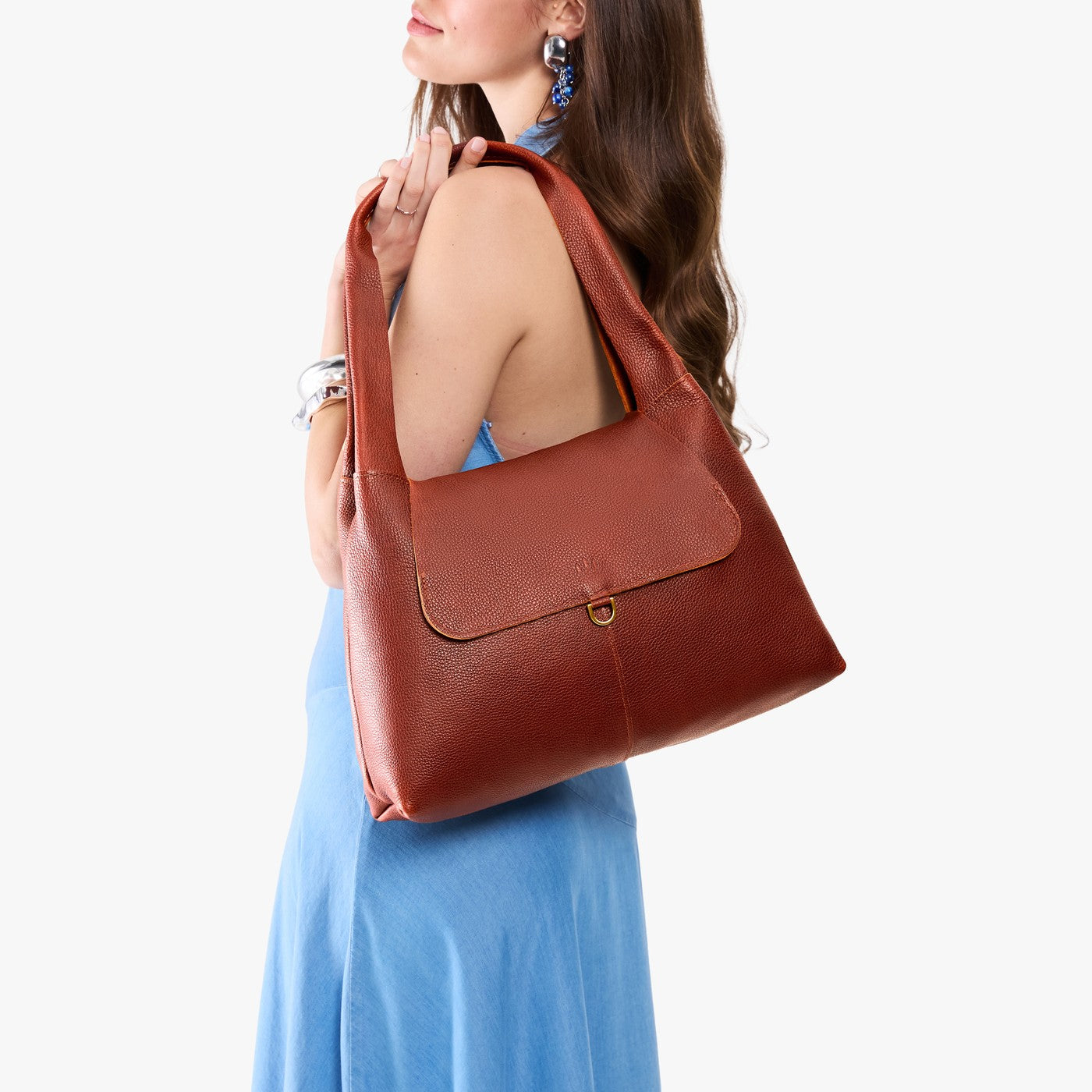 Nutmeg*Medium | A model holding a slouchy triangle shaped shoulder bag with a flap