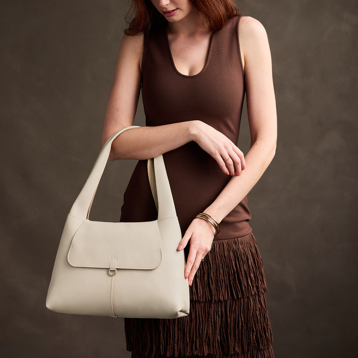 Pebbled Bone*Medium | A model holding a slouchy triangle shaped shoulder bag with a flap