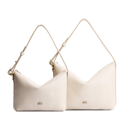 Pebbled Bone | Size comparison shot of small and large slouchy leather shoulder bags with zipper opening and three metal tree emblems