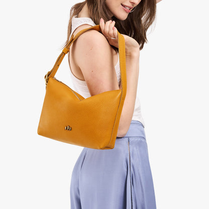 Sunshine*Small | Model holding a Slouchy Shoulder Bag that has a zipper opening and three metal tree emblems