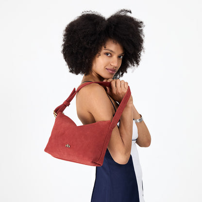 Cinnabar*Small | Model holding a Slouchy Shoulder Bag that has a zipper opening and three metal tree emblems