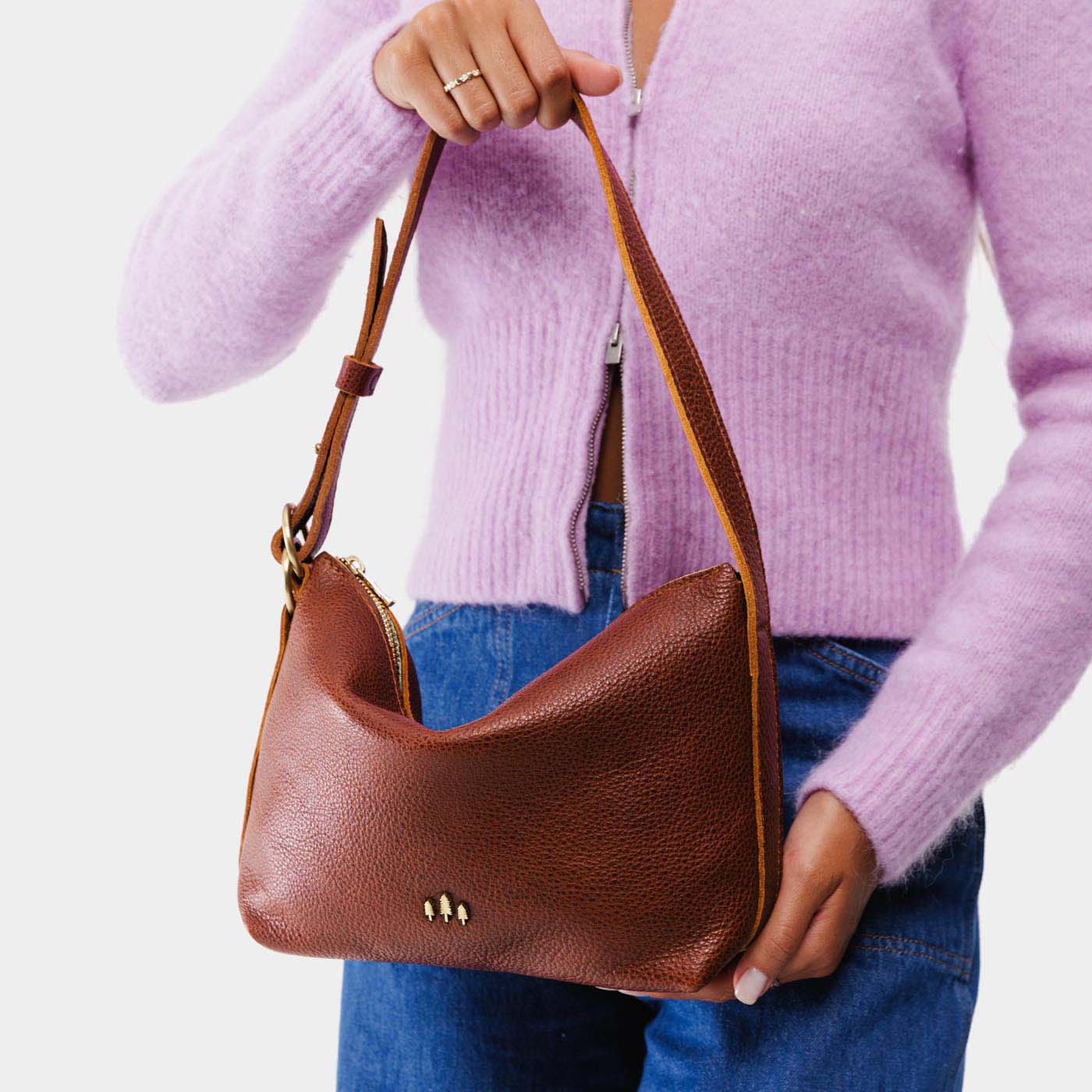 Nutmeg*Small | Model holding petite slouchy leather shoulder bag with zipper opening and three metal tree emblems
