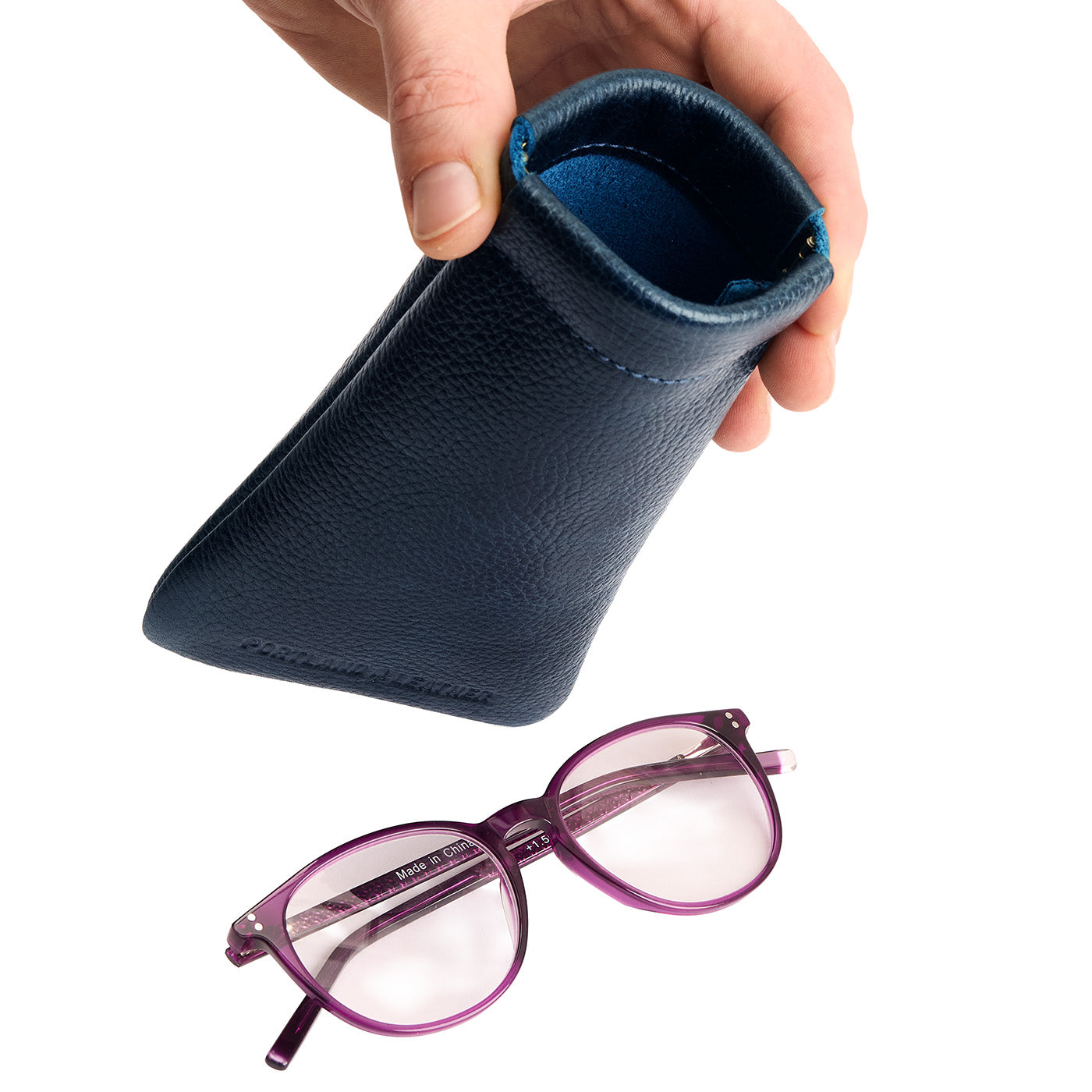 Boreal | Model hand holding open leather glasses case with hidden metal spring closure above a pair of glasses