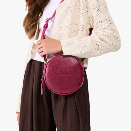 Orchid | Model wearing a circle shaped crossbody bag with top zipper and gold accents