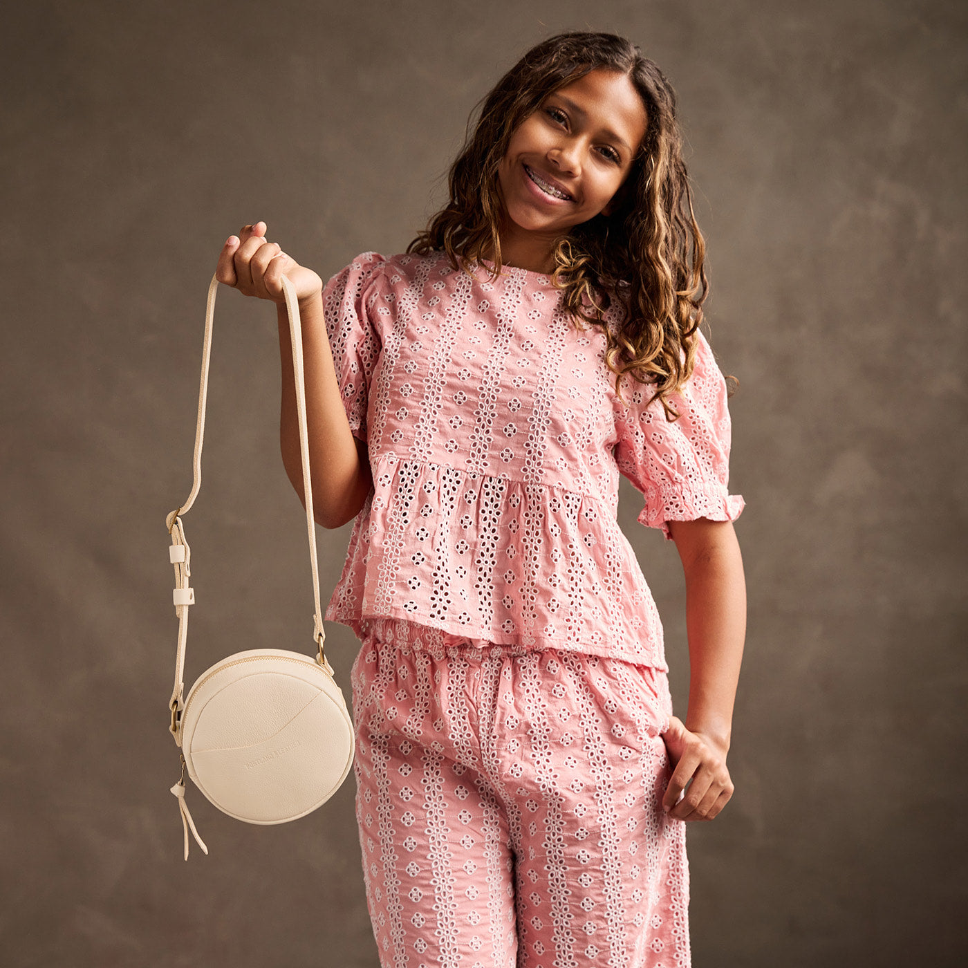 Pebbled Bone | Model holding a circle shaped crossbody bag with top zipper and gold accents