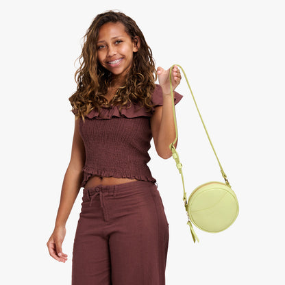 Shadow Lime | Model holding a circle shaped crossbody bag with top zipper and gold accents
