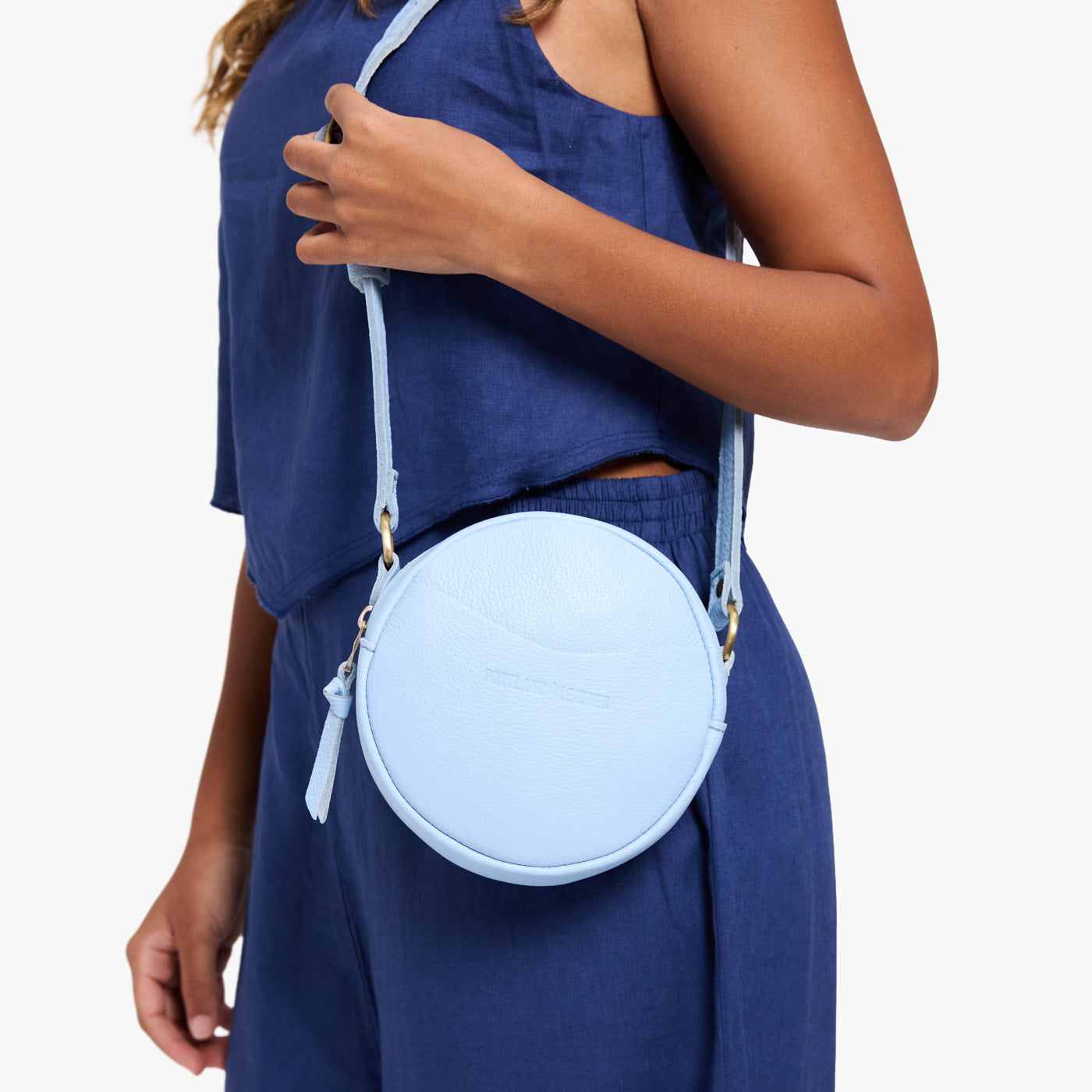 Skyway | Model wearing a circle shaped crossbody bag with top zipper and gold accents