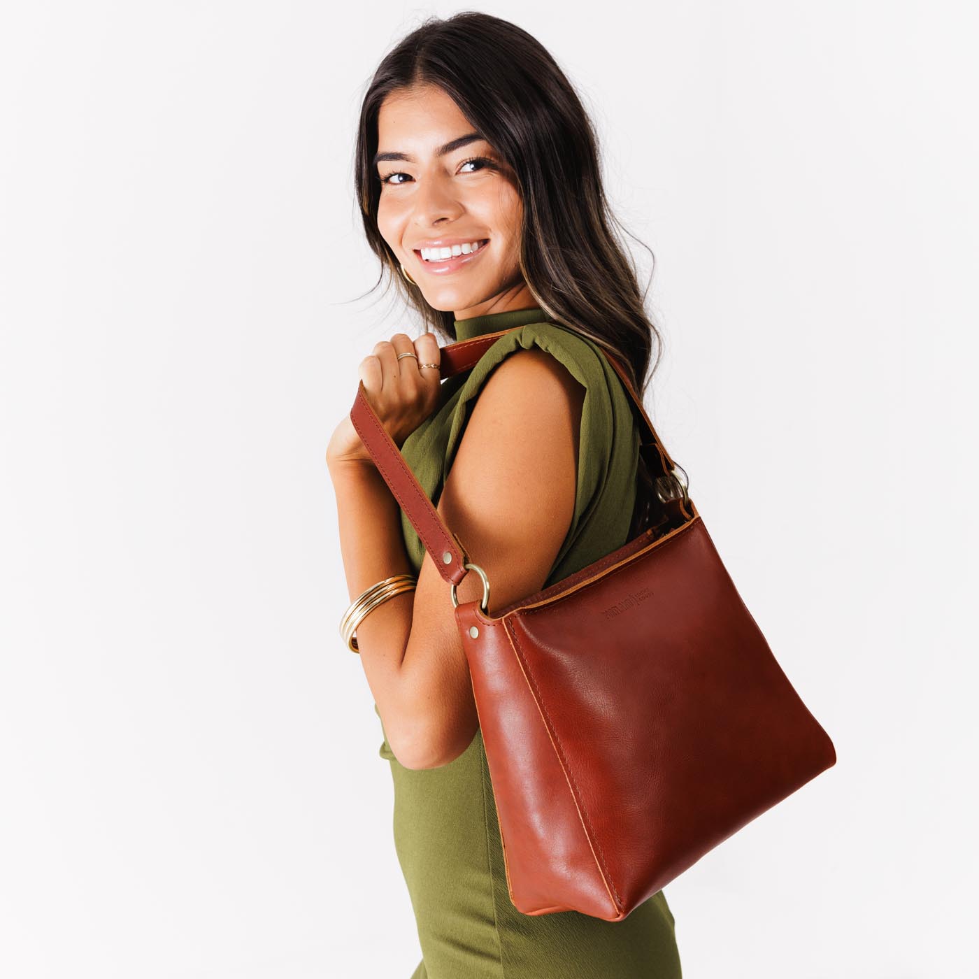 Chestnut*Small | Model carrying leather triangular shoulder bag with zipper top closure and wide shoulder strap
