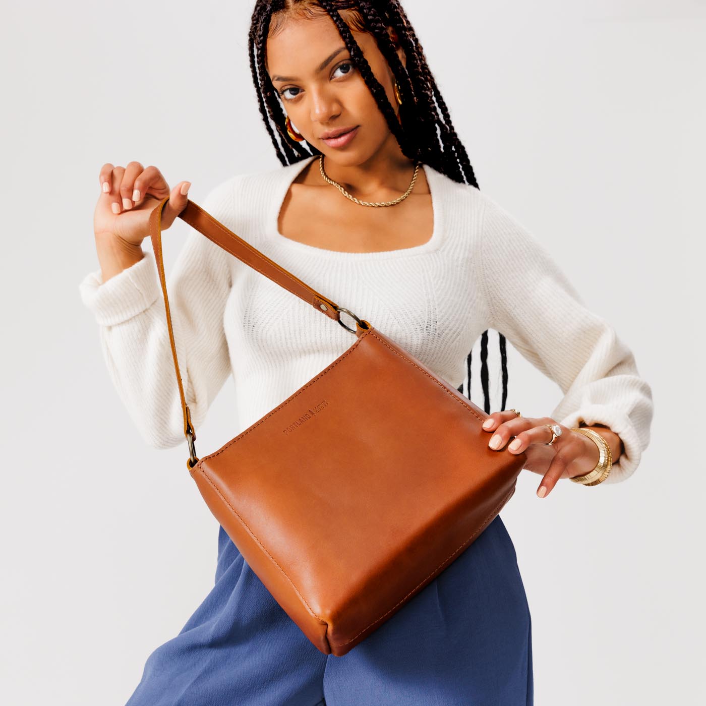 Honey*Classic | Model holding leather triangular shoulder bag with zipper top closure and wide shoulder strap