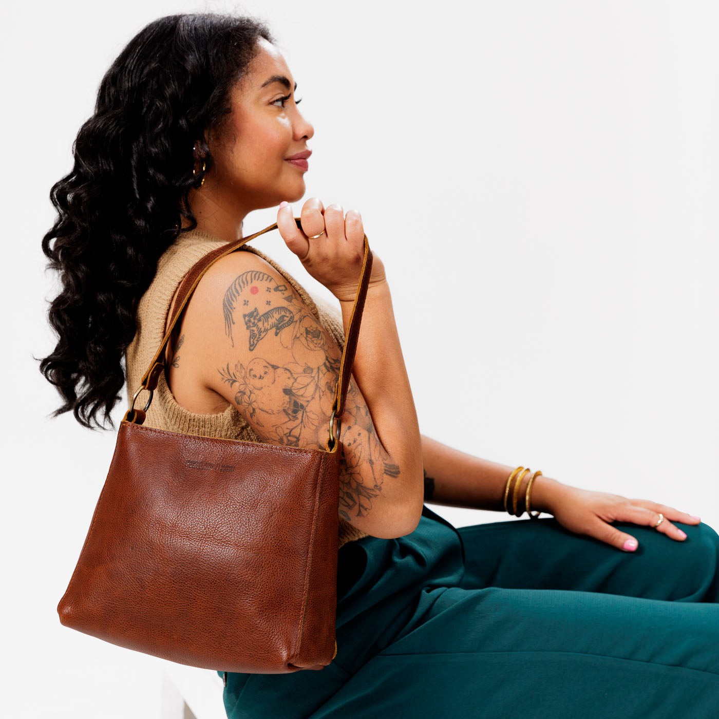 Nutmeg*Classic | Model holding leather triangular shoulder bag with zipper top closure and wide shoulder strap