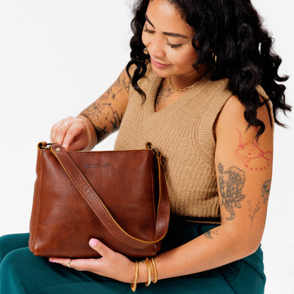Nutmeg*Classic | Model holding leather triangular shoulder bag with zipper top closure and wide shoulder strap