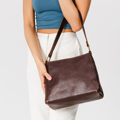 Coldbrew*Classic | Model holding leather triangular shoulder bag with zipper top closure and wide shoulder strap