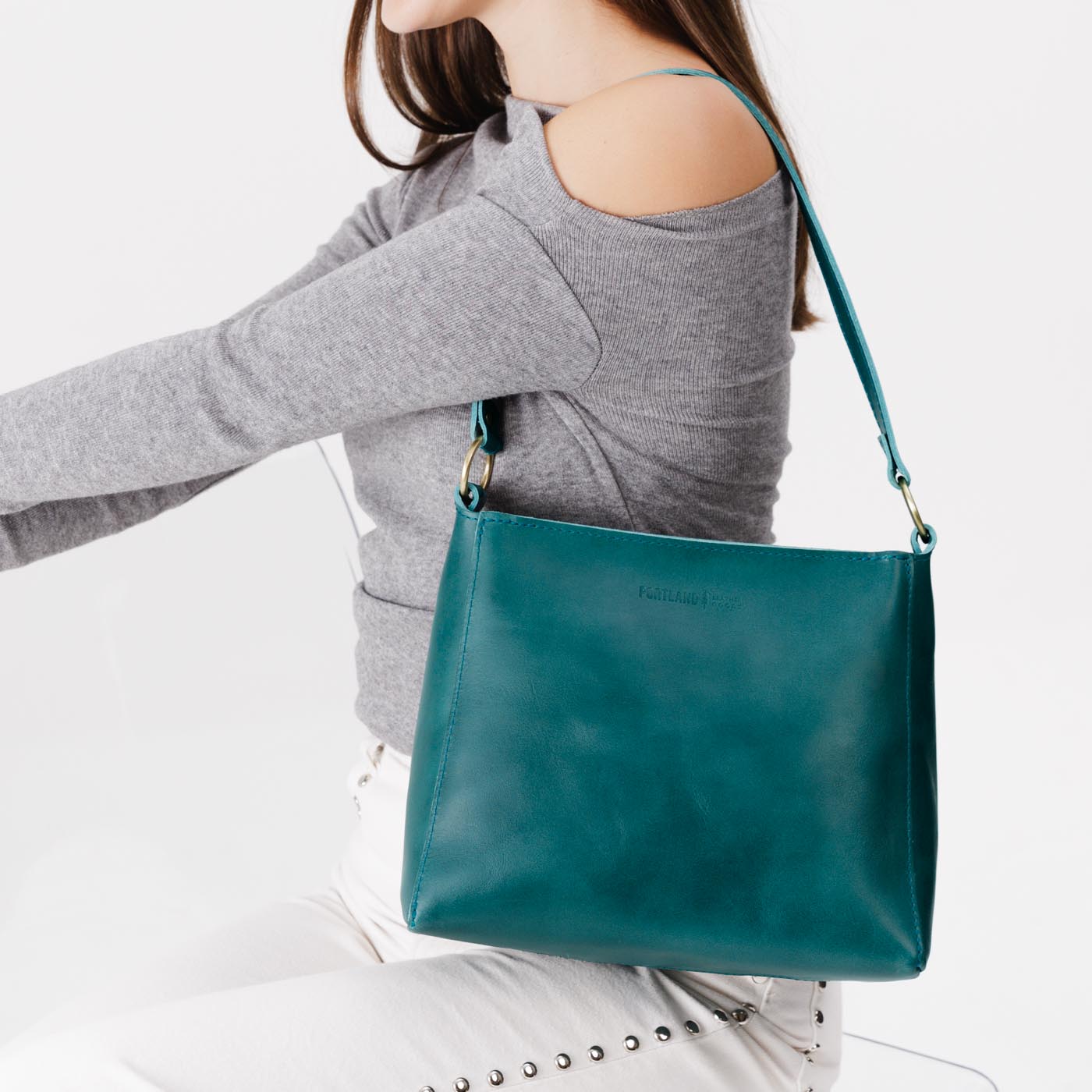 Caribbean*Small | Model carrying leather triangular shoulder bag with zipper top closure and wide shoulder strap