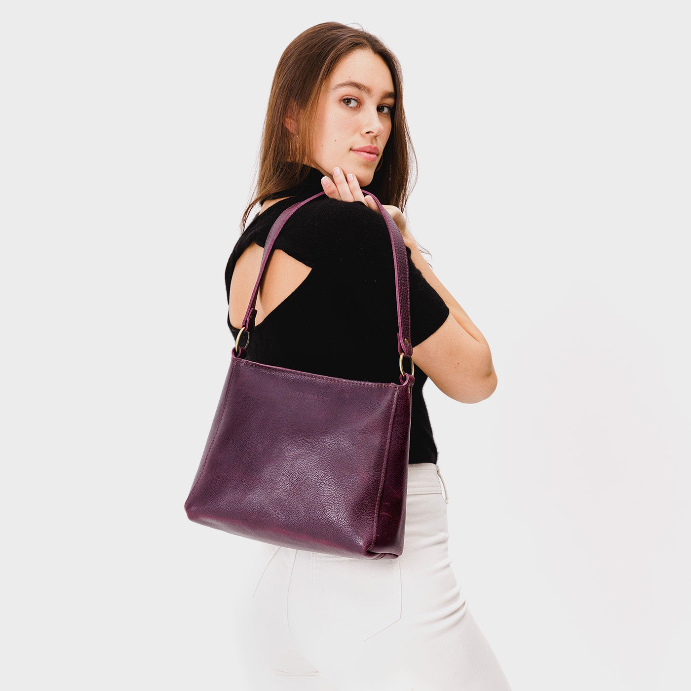 Plum*Classic | Model carrying leather triangular shoulder bag with zipper top closure and wide shoulder strap