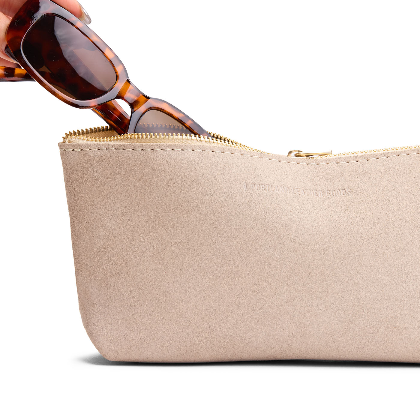 Taupe | Model hand pulling pair of sunglasses from leather utility bag pouch with top zipper